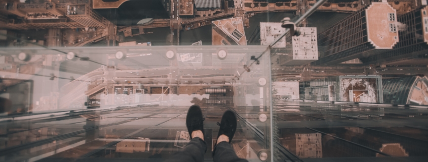 Person standing on glass floor overlooking city below